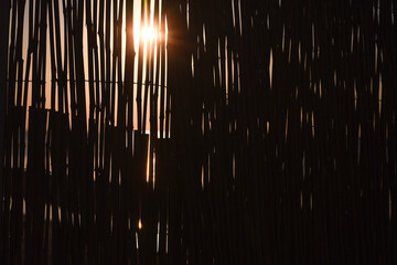Obraz premium Sunlight shining through vertical bamboo slats, creating dramatic light and shadow patterns, warm glow, abstract natural texture, outdoor environment, artistic and moody atmosphere.