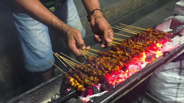 Grilling chicken satay skewers over charcoal at night street food stall