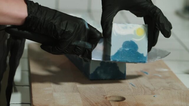 Strong hands of woman with large knife quickly cut large bar of soap into small pieces intended for sale