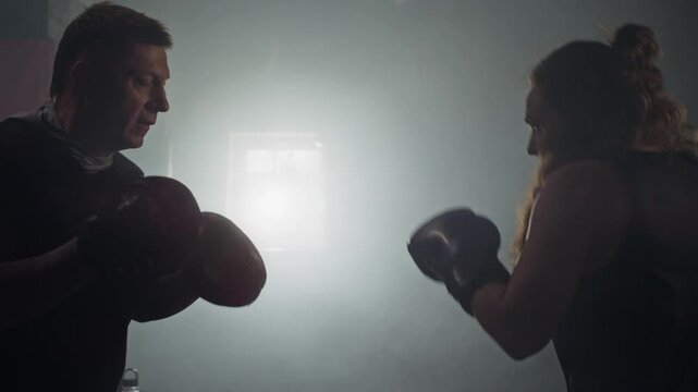 Young Caucasian woman practicing boxing punches with middle-aged Caucasian trainer holding focus mitts. Clip suitable for fitness brand advertisements and gym promotional videos