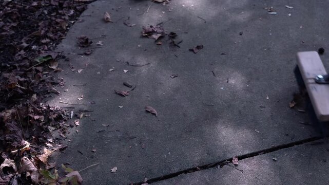 Person sweeping dried autumn leaves off concrete sidewalk with wooden push broom.