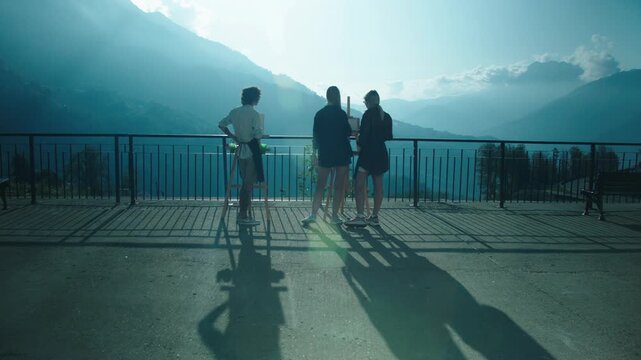 Artists and spectator against backdrop of mountain landscape. Preparation for watercolor painting. Mountains, clouds, valley, road. Teacher watches student.