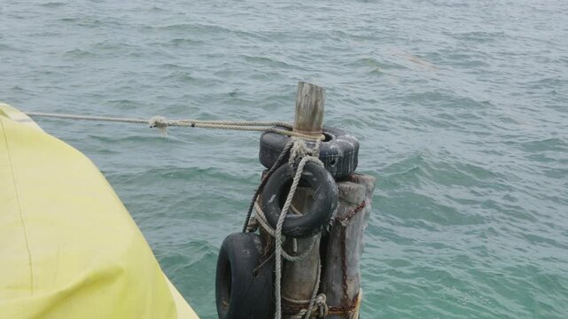 Yellow boat hull tethered to a rustic wooden dock piling with old tires in the rippling ocean