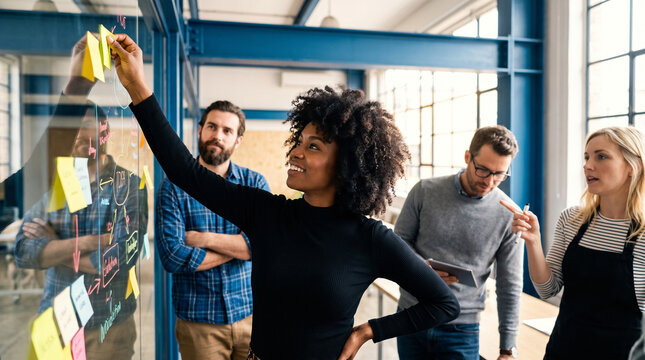Diverse business team collaborating on glass board with sticky notes in modern office setting