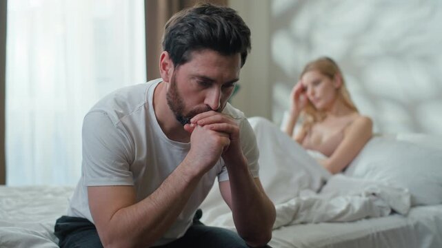 Disappointed Caucasian man husband thinking solution holding head separated near offended woman wife in bedroom. Couple family quarrel misunderstanding marriage divorce breakup intime problem in bed