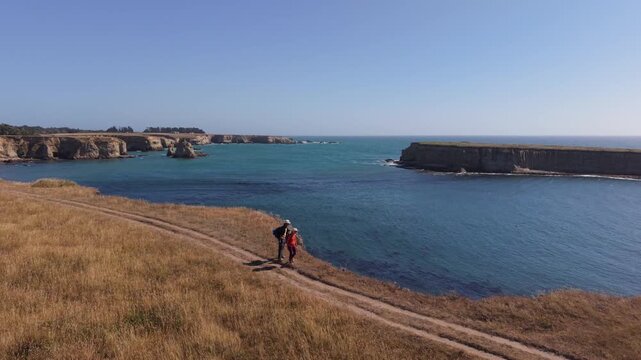 Man and woman walk together on a trail overlooking the ocean at Point Arena near Mendocino, California on a clear day.