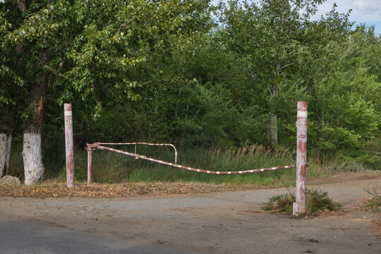 Old rusty metal barrier gate blocking dirt road entrance in lush green countryside forest.