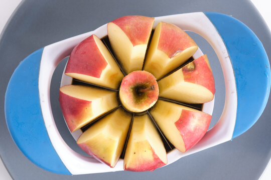 Top view close up red apple being sliced with blue plastic apple corer slicer tool.