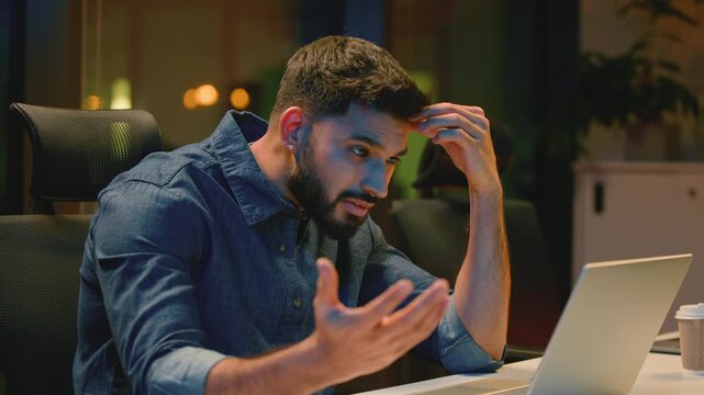 Troubled puzzled Indian business man with laptop frustrated at dark night office Arabian businessman male guy worker feeling stress with online work problem computer failure overworked at late evening