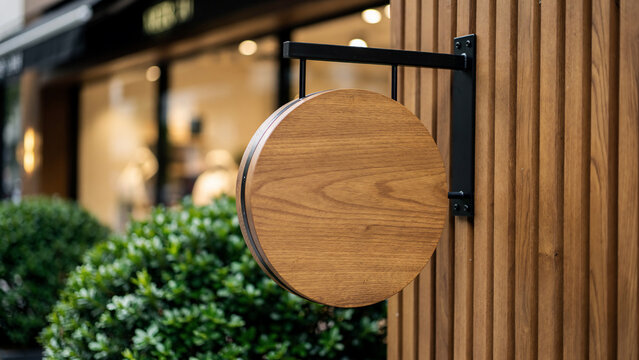 Wooden round sign with black metal bracket mounted on a ribbed wooden pole, blurred shop front in background, concept for business branding, store signage and retail display advertising