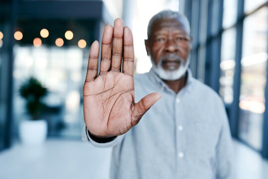 Serious senior man with an open palm gesture signaling stop or caution in an office environment, conveying a firm boundary or warning.