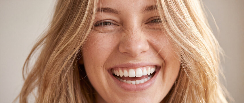 Close up portrait of laughing blonde woman featuring genuine smile, soft natural lighting, and warm beige tones for skincare, dental health, beauty care, and wellness visual advertising