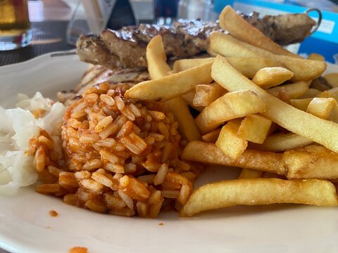 Echtes Foto eines griechischen Grilltellers mit Pommes frites, Fleischspie&szlig;en, Hacksteak und Beilagen im Restaurant. Typische mediterrane K&uuml;che, Urlaub und herzhafter Genuss.