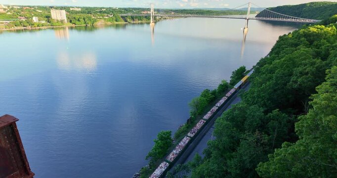 Large suspension bridge spanning across a wide calm Hudson River with forested shores