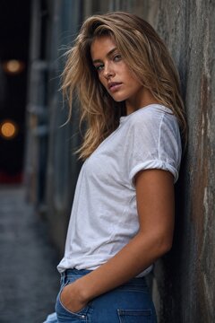 Fashion model posing against a textured wall with dramatic urban ambiance.