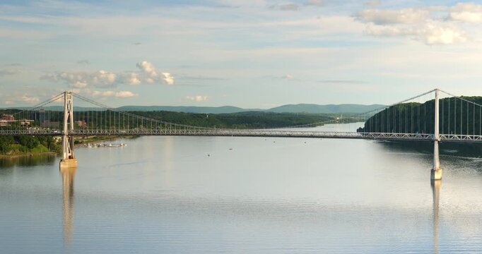 Large suspension bridge spanning across a wide calm Hudson River with forested shores