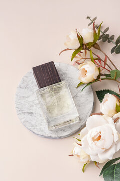 Glass perfume bottle on a round marble podium with floral decoration on a pastel beige background