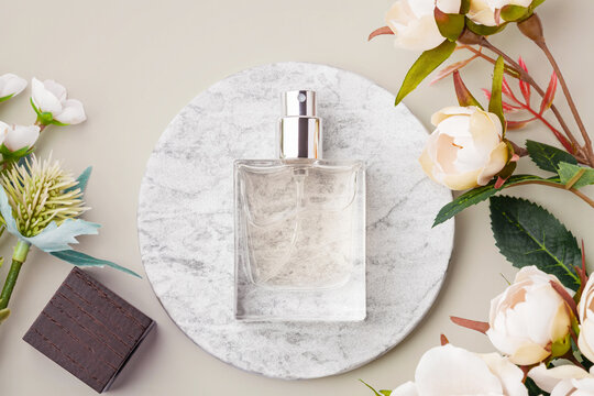 Glass perfume bottle mockup on a round marble podium with floral decorations on a pastel neutral background