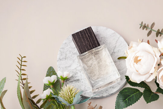Glass perfume bottle on marble tray with decorative roses and green leaves on a pastel beige background