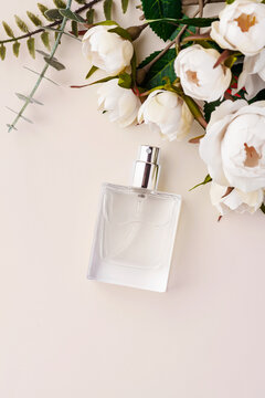Transparent glass perfume bottle with rose decorations on a pastel pink background