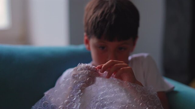 Boy popping bubble wrap at home, highlighting sensory play, focus and stress relief