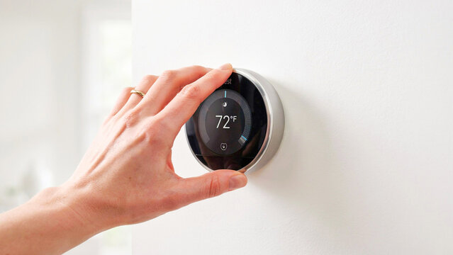 Close-up of a hand adjusting a smart thermostat displaying 72 degrees, indicating home climate control and energy efficiency