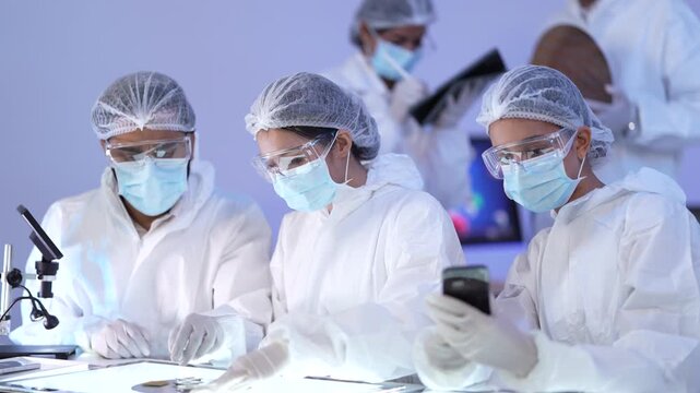 Cleanroom scientists in coveralls and masks lean over an illuminated light table to examine and compare small samples during a sterile laboratory quality inspection