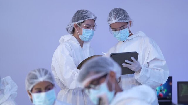 Semiconductor engineers in cleanroom suits inspect a round silicon wafer alongside a tablet during a microchip quality check in a sterile hitech manufacturing facility