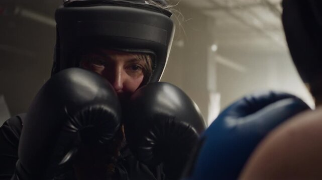 Young Caucasian woman wearing headgear sparring in boxing ring, throwing punches at opponent. Footage ideal for women empowerment campaigns and fitness brand advertisements
