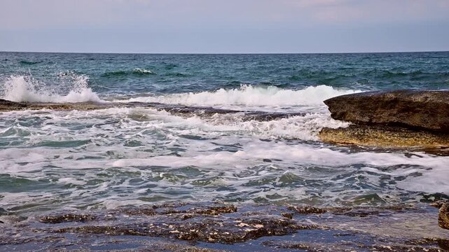 Waves crashing against rocky shore, creating foam and splashes in ocean