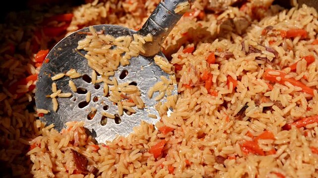 Rice dish preparation with metal spatula scooping flavorful pilaf mixture