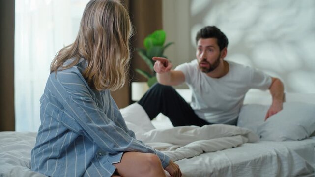 Caucasian couple spouses arguing quarrel conflict in bedroom. Angry husband yelling with rage argue with annoyed wife on bed irritated wife with jealous man fighting pushing family problem violence