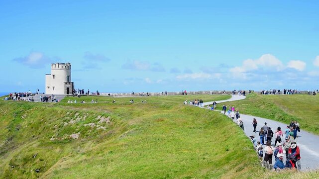 County Clare, Ireland - June 20, 2026: Tourists walk along the coastal path toward O'Brien's Tower at the Cliffs of Moher.