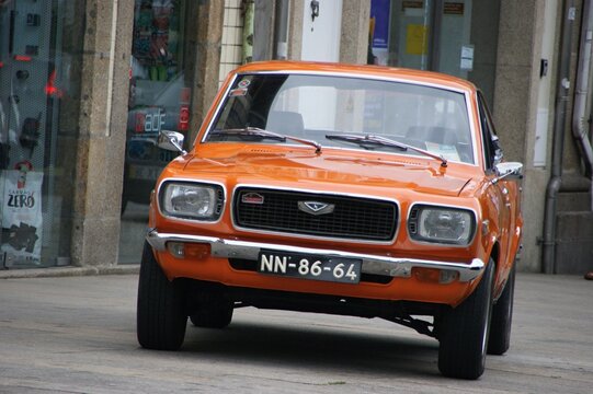 Orange Mazda 808 vintage car driving on urban street
