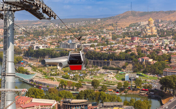 Cable car crossing above Rike Park with panoramic city views and the Holy Trinity Cathedral in Tbilisi, Georgia.