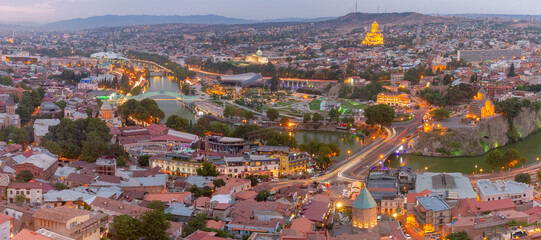Panoramic view of Tbilisi city center with illuminated bridges, churches, the Kura River and modern architecture at dusk in Georgia. © Kavalenkava