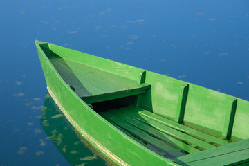 Bright green wooden boat floating on calm blue water, a simple lakeside scene suited to boating, outdoor leisure, travel and tranquility themes. © Jacek