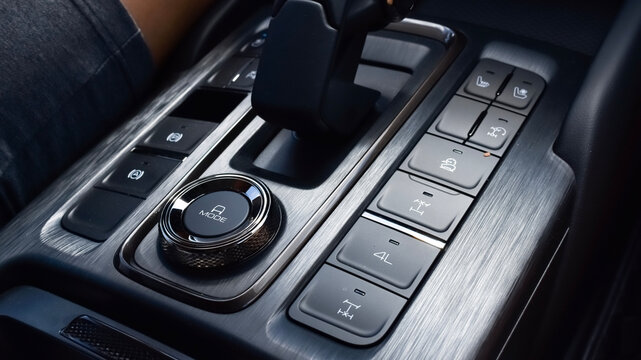Close-up of a modern SUV center console featuring automatic gear lever, drive mode selector knob, 4WD buttons, electronic parking brake, and brushed metal trim