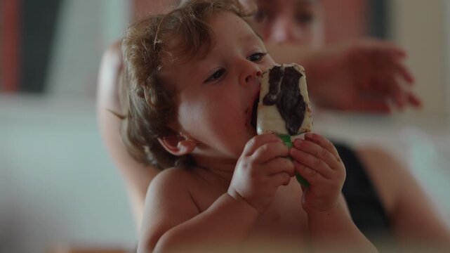 Toddler eating chocolate coated ice cream, highlighting self feeding, childhood enjoyment and everyday family life