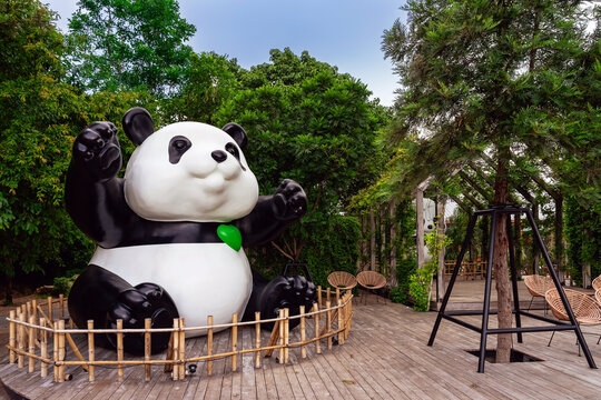 KANCHANABURI, THAILAND - JUNE 12, 2026: A large cute giant panda statue holding green heart balloons on wooden deck with lush green ivy wall background at CHAN nature cafe (local tourist attraction).