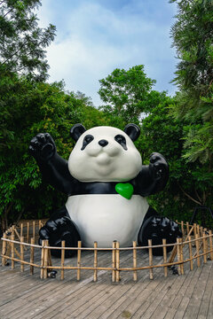 KANCHANABURI, THAILAND - JUNE 12, 2026: A large cute giant panda statue holding green heart balloons on wooden deck with lush green ivy wall background at CHAN nature cafe (local tourist attraction).