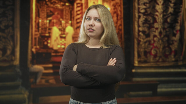Blonde woman with folded arms and a grimace, standing before an ornate altar with robed priests in a church interior; disgust defiance.