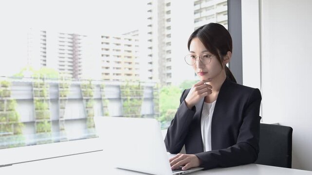 ノートパソコンを使って仕事をする眼鏡姿の20代日本人女性