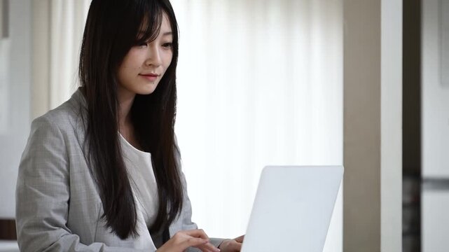 ノートパソコンを操作して微笑む20代日本人女性