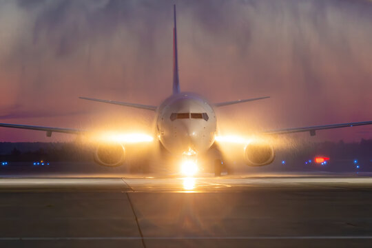 Front view of a white passenger plane passing through a water arch at night