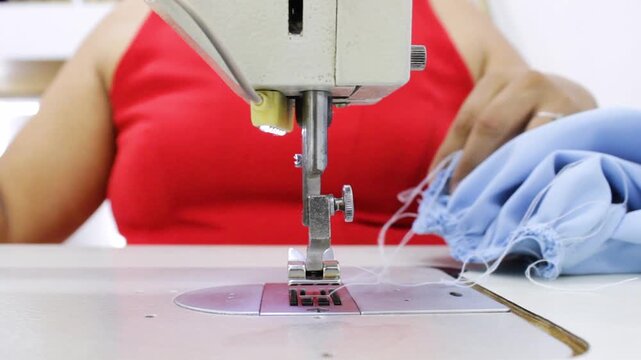 A seamstress's hands are hemming an elegant blouse on a sewing machine and then cutting the garment with scissors at her workstation inside a textile factory in Neiva, Huila, Colombia