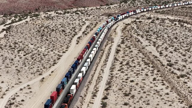 Aerial view of long freight container trains passing each other on desert railway tracks