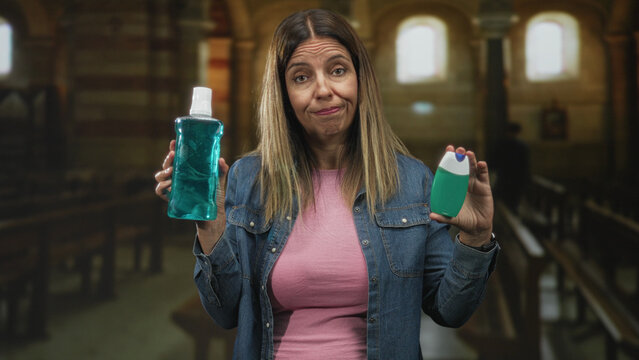 Woman holding mouthwash bottle and toothpaste tube, holds both products up with a puzzled squint and shrugged shoulders in a church pew aisle; indecision.