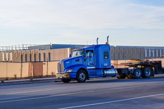 Flatbed semi truck passes a large data center campus under construction, illustrating freight transportation, logistics, AI infrastructure, and commercial development