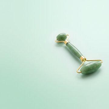 Green jade facial roller with gold accents on pastel background